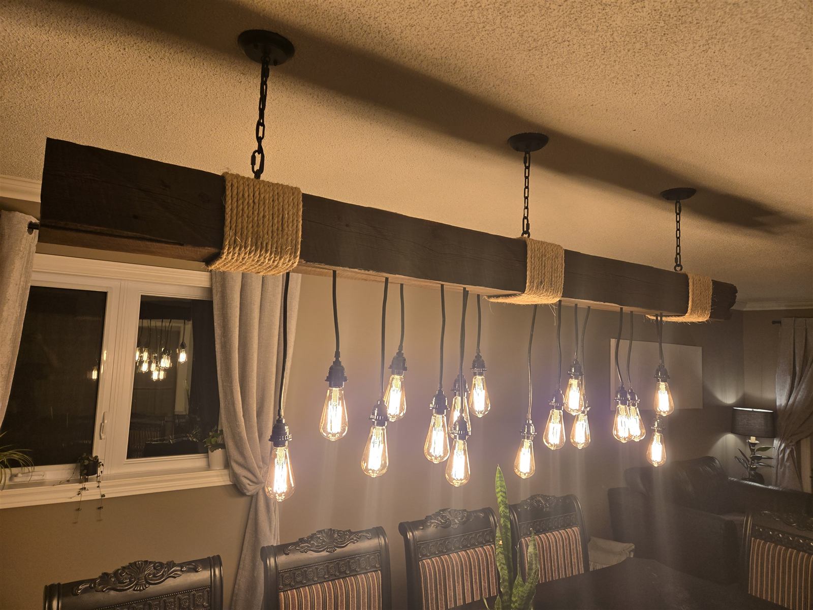 Wood light fixture spanning a dining table, rope-wrapped mounting bands, staggered hanging bulbs